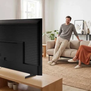 Deux personnes sont assises sur un canapé, souriantes, et regardent un grand téléviseur SAMSUNG TU50M74H dans un salon lumineux et moderne.