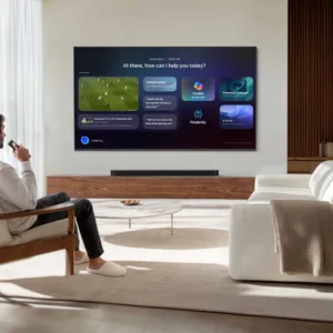 Un homme est assis sur un canapé, une télécommande à la main, et regarde son téléviseur SAMSUNG TU50M74H qui affiche plusieurs applications, dans un salon moderne.