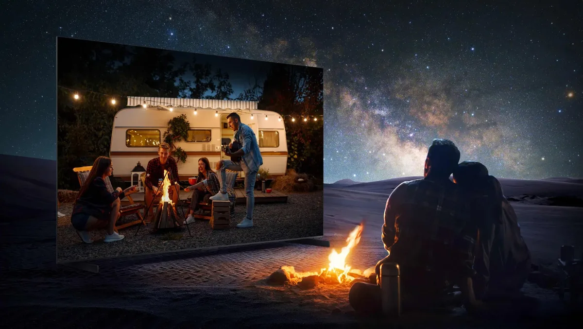 Un couple prend plaisir à regarder, sur son téléviseur TCL 65C8L, une image projetée représentant des amis autour d'un feu de camp, sous un ciel étoilé.