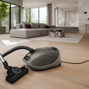 L'aspirateur Miele GUARD M1 SILENCE, doté de la technologie SILENCE, est posé sur un parquet dans un salon moderne agrémenté d'un canapé gris et de grandes fenêtres.