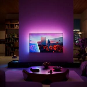 Un téléviseur PHILIPS 55OLED851 (Copie) fixé au mur, doté d'un rétroéclairage violet, illumine le salon moderne la nuit et offre une vue imprenable sur la ville.