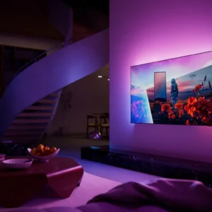 Un salon contemporain mettant en vedette un téléviseur OLED PHILIPS 55OLED851 (Copie) aux couleurs éclatantes, fixé au mur, baigné d'un éclairage d'ambiance violet, avec un escalier en colimaçon visible à l'arrière-plan.