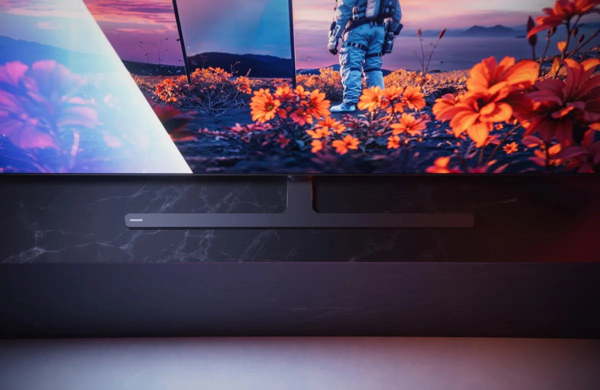Un téléviseur OLED PHILIPS 55OLED851 (Copie) affiche l'image d'un astronaute dans un champ de fleurs orange, avec une barre de son noire placée sous l'écran.