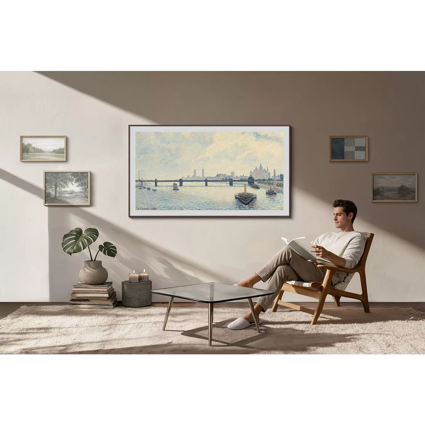 Un homme est assis sur une chaise et lit dans un salon moderne orné de tableaux encadrés aux murs, d'une table basse et d'un téléviseur SAMSUNG TQ55LS03HW THE FRAME qui s'intègre parfaitement au décor.