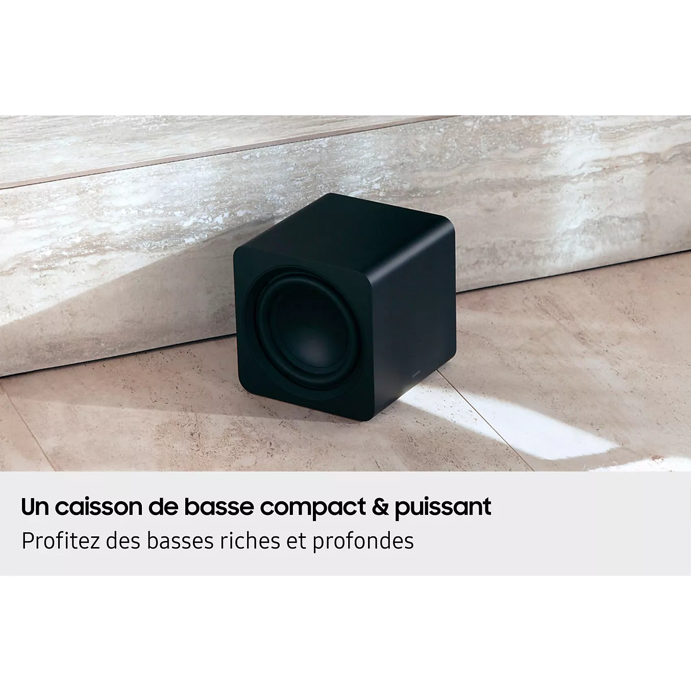 Le SAMSUNG HW-Q930H, un caisson de basses compact noir issu d'un système home cinéma, est posé sur un sol de couleur claire, près d'un mur, avec un texte en français affiché en dessous.