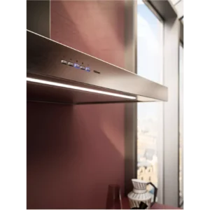 La hotte en acier inoxydable FALMEC PLANEP1430, dotée de boutons de commande et installée sur un mur de cuisine de couleur mauve près de grandes fenêtres, est l'appareil de cuisine moderne par excellence.